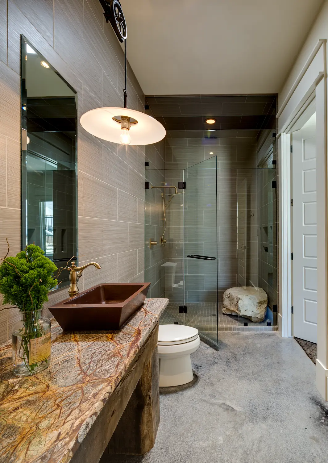 Bathroom with a copper vessel sink on a stone counter and a glass shower