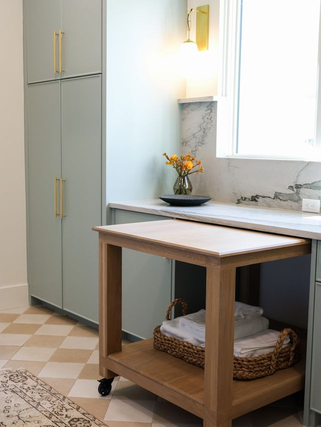 Laundry room with checkerboard tile floor, sage cabinetry, and a white oak rolling cart
