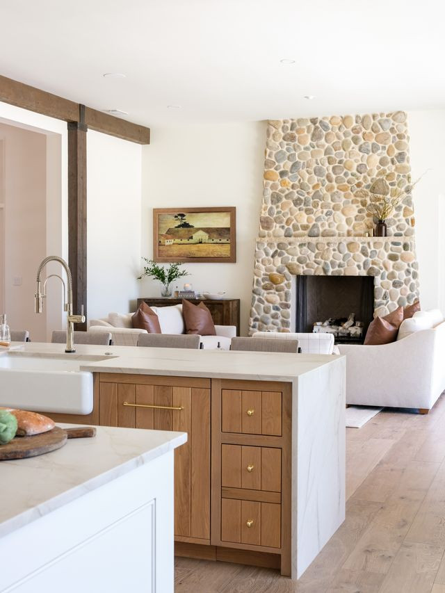 Open kitchen and living room with white oak island, marble counters, and a river-rock fireplace