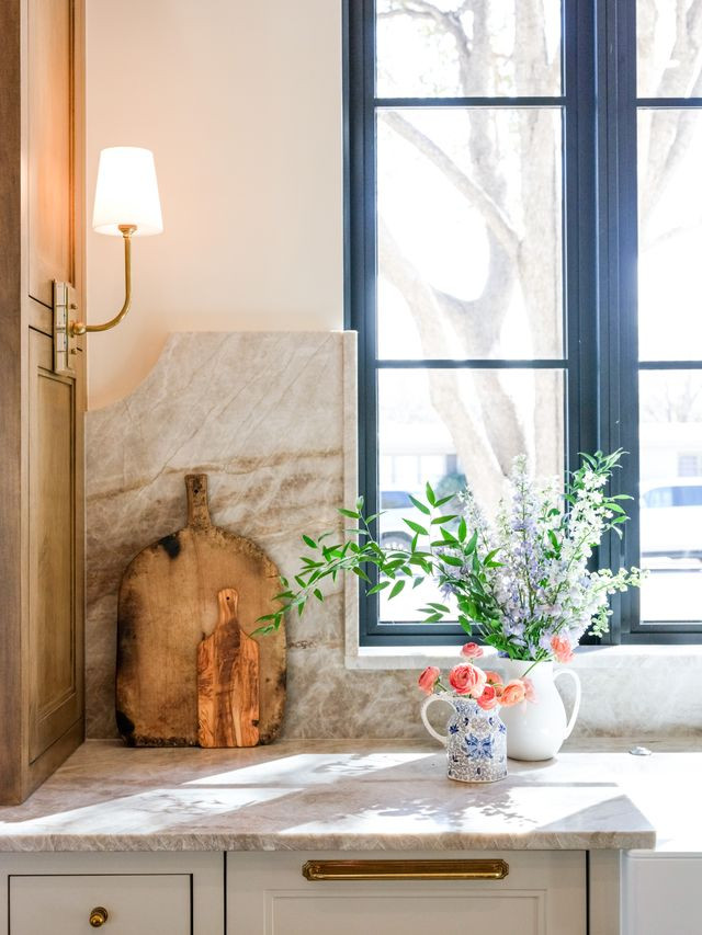Kitchen window with quartzite backsplash, brass sconce, and fresh flowers