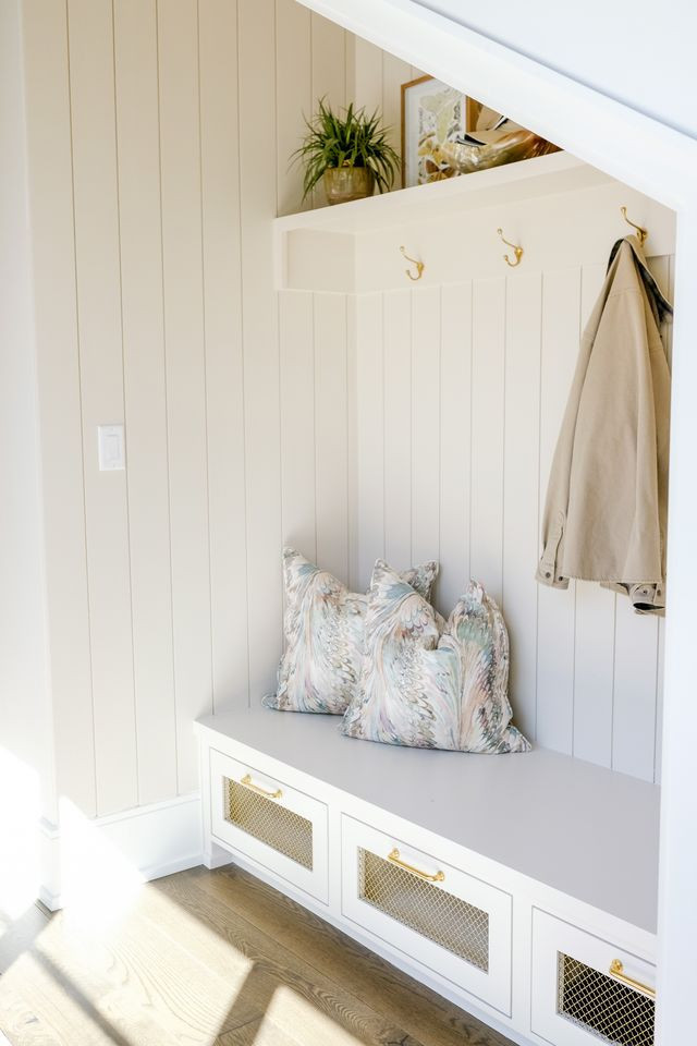Mudroom nook with vertical shiplap, brass hooks, and a bench with wire-front drawers